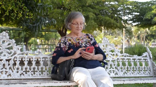 Senior woman sitting on a park bench checking her cellphone