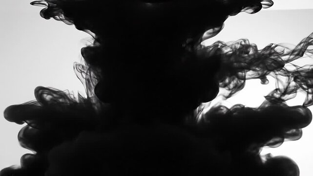 Black ink swirling in water creating abstract smoke-like patterns on white background