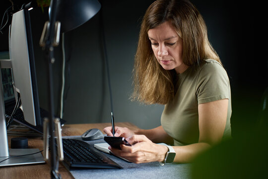 Woman using smartphone while working at home office desk