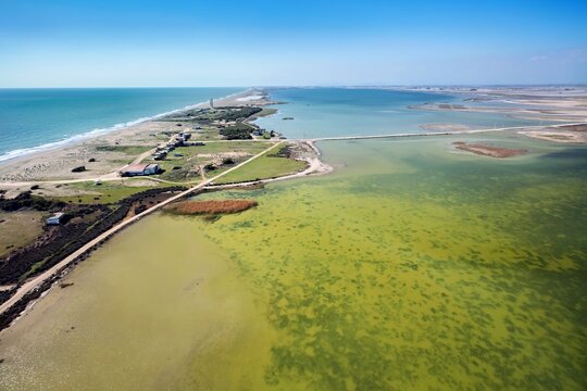 Aerial view of Tuzla Lagoon featuring a narrow strip of land separating the calm green waters from the Mediterranean Sea, with sandy beaches and sparse vegetation in Karatas, Adana, Turkey.
