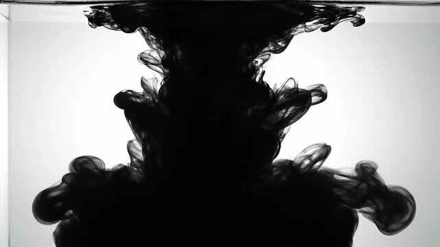 Black ink swirling in clear water creating abstract smoke shapes with fluid motion on white background