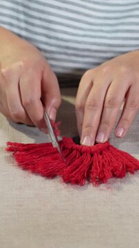 Female hands crafting with red thread while smoothing the fibers