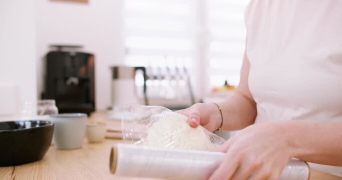 Preparing food. Dough recipe. Female chef hand wrapping white raw mass covering with plastic culinary film roll on kitchen counter.