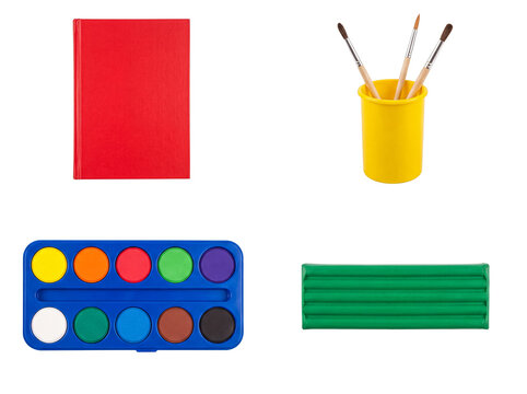 Variety of colorful art and school supplies: red book, paintbrushes in cup, watercolor palette, and green clay.