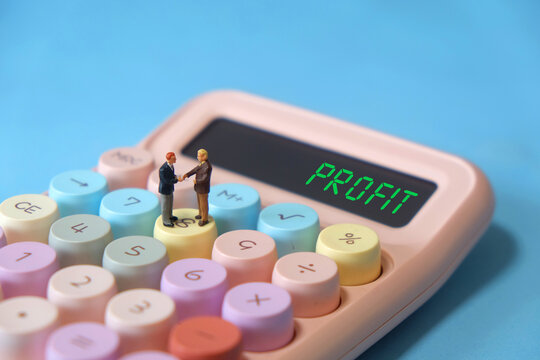 Miniature business partners shaking hands on calculator with PROFIT text on display, business success concept