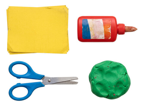Rustic children's craft supplies flat lay, with worn yellow paper, old glue, blue scissors, and green playdough.