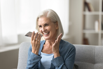 Naklejka premium Voice app. Cheerful excited elderly woman grandmother hold smartphone by mouth dictate request to virtual assistant record vocal message. Happy aged lady use phone loudspeaker for easy communication