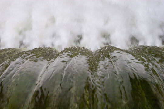 Fast-moving water pouring over a concrete dam edge, creating smooth crests and white foam below.