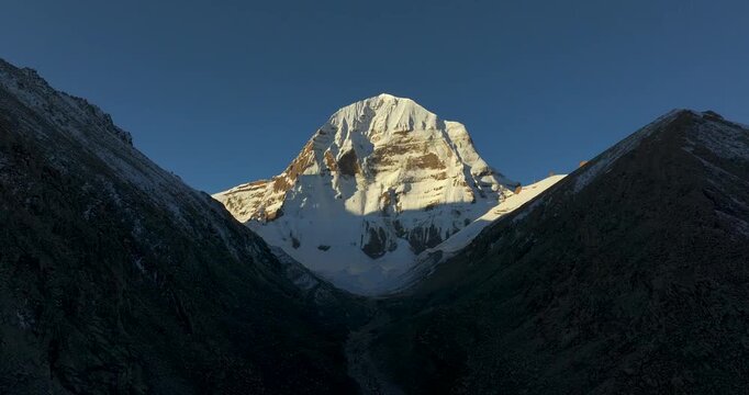 Aerial shot of sacred Mount Kailash peak, Tibet, China, illuminated by golden sunrise light along the kora circuit underneath the blue sky