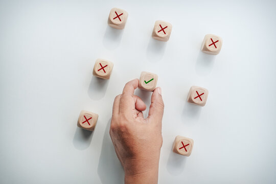 Hand selecting wooden block with green checkmark among red cross mark blocks, concept of correct choice, right decision, quality control, success, and problem solving.