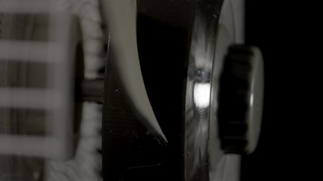Oscillating fan blades move behind a metal grille in dim indoor light.