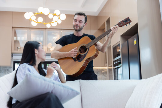 Young multicultural couple enjoying live acoustic guitar music together in a bright modern home. Romantic relationship