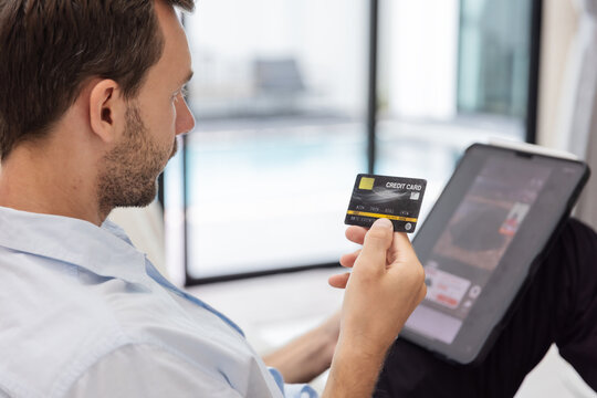 Young man holding a credit card while using a laptop to make an online purchase from home. E-commerce checkout, secure digital payment, internet banking, cashless transaction and consumer technology .