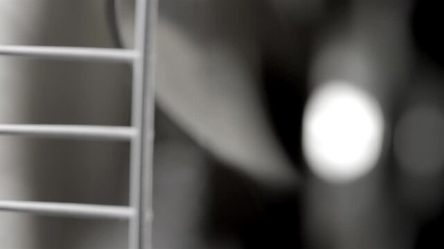Oscillating fan blades turn behind a silver grille in soft focus indoors.