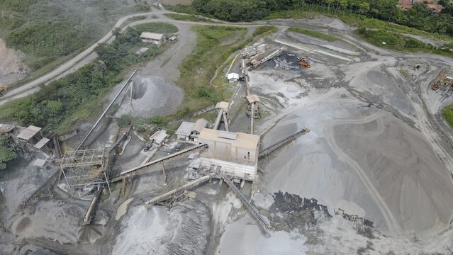 Aerial view of a stone quarry mining site with conveyor belts, piles of crushed rock, and industrial processing machinery in Rumpin, West Java, Indonesia.
