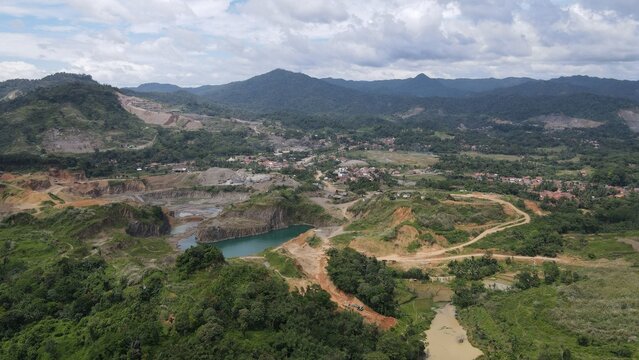 Aerial view of a quarry with turquoise water surrounded by lush green hills and dirt roads in Rumpin, West Java, Indonesia.