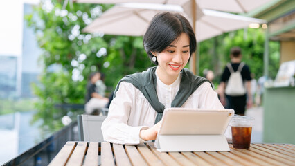 Fototapeta na wymiar Beautiful smiling adult business asian woman relax at outdoor terrace of cafe with coffee drink and digital tablet on table
