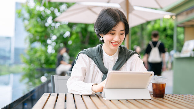 Beautiful smiling adult business asian woman relax at outdoor terrace of cafe with coffee drink and digital tablet on table