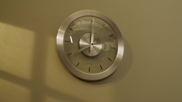 Modern wall clock showing time passing with minimalist design and silver frame on beige wall.