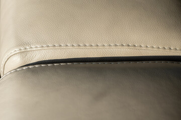 Close up detail of beige leather upholstery with visible stitching and curved seam on modern furniture.  © Marek