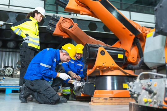 Robotics engineer and technician repairing industrial robot arm in factory plant, automation team maintaining and servicing robotic machinery at manufacturing, workers working on robotic arm system