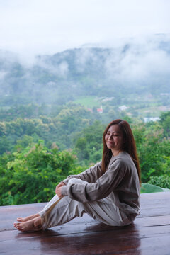 Vertical image of a woman sitting on wooden balcony with a beautiful mountain views on cloudy morning