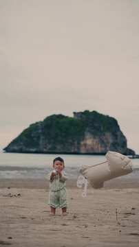 Vertical shot of Asian baby boy playing with number 1 balloon on beach for first birthday.