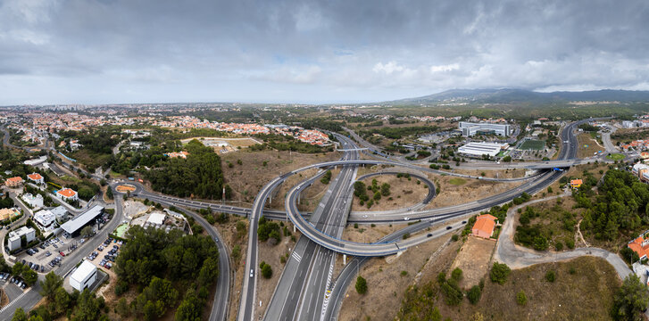 Aerial view of the A5 highway interchange surrounded by urban development, green spaces, and trees in Cascais, Lisboa, Portugal.