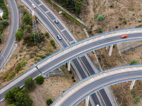 Aerial view of the A5 highway interchange with multi-level overpasses, concrete supports, and vehicles driving on asphalt roads surrounded by dry vegetation in Cascais, Lisboa, Portugal.