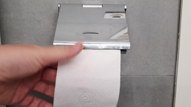 Hand taking toilet paper roll in bathroom closeup.