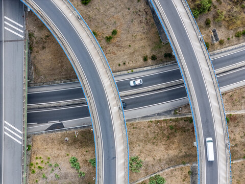 Aerial view of the A5 highway interchange with curved overpasses and vehicles driving on the asphalt roads in the dry landscape of Cascais, Lisboa, Portugal.