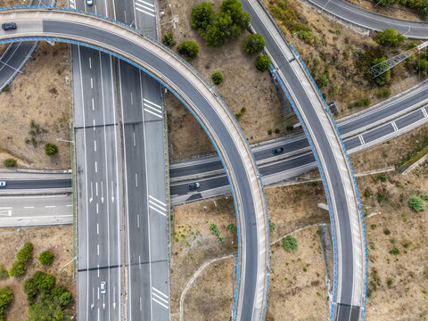 Aerial view of the A5 highway interchange with curved overpasses and multiple lanes surrounded by dry landscape in Cascais, Lisboa, Portugal.