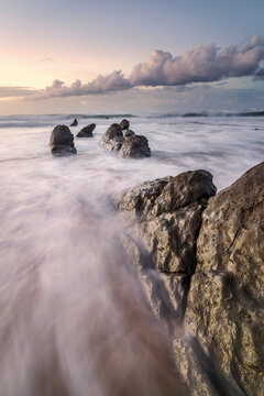 Flysch rock formations sticking out from the wet sand on the beach of Barrika at sunset with low shutter speed water motion, Basque Country, Spain
