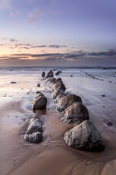Flysch rock formations sticking out from the wet sand on the beach of Barrika at sunset with low shutter speed water motion, Basque Country, Spain