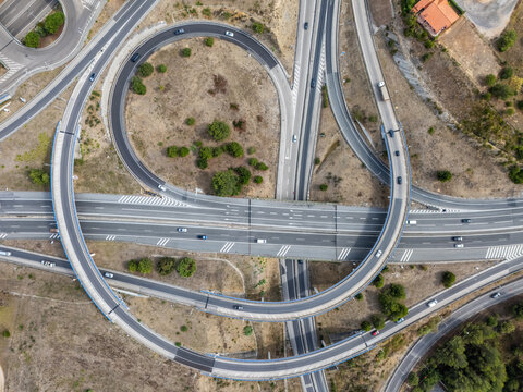 Aerial view of the A5 highway interchange featuring curved ramps and multi-lane roads with vehicles driving through a dry landscape in Cascais, Lisboa, Portugal.