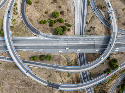 Aerial view of A5 highway interchange with curved ramps, multiple lanes, and surrounding dry landscape in Cascais, Lisboa, Portugal.