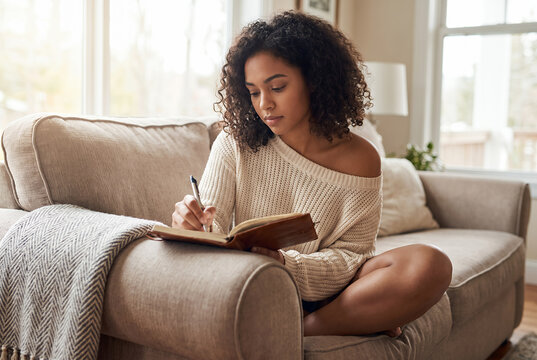 African American woman writing in notebook on comfortable sofa