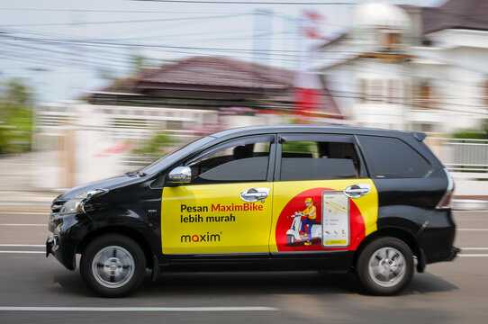 Riau-Indonesia, august 25th 2026 : a black passenger car featuring official yellow and red side branding for the ride-hailing and delivery service Maxim