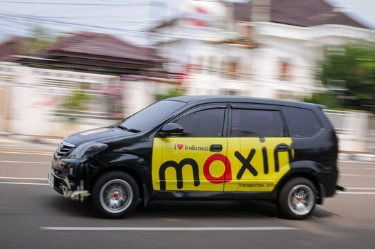 Riau-Indonesia, august 25th 2026 : a black passenger car featuring official yellow and red side branding for the ride-hailing and delivery service Maxim