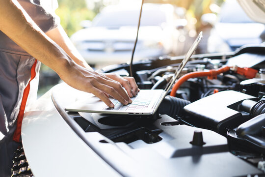 Professional car mechanic hands using laptop computer for diagnostic checking system and vehicle performance analysis during engine service maintenance in auto repair workshop garage.
