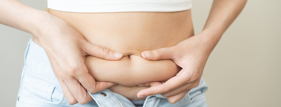 Weight gain, overweight, high cholesterol and pressure, woman hand pinching excess fat big belly with finger and wear tight trousers, show fat around abdomen body, getting loss, isolated on background