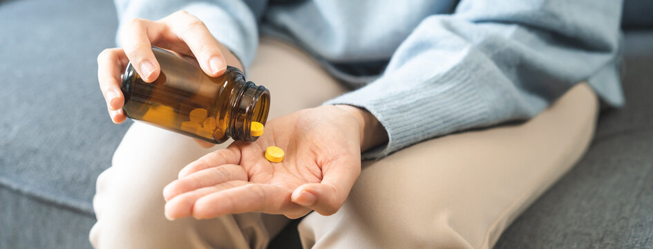 Sick, ill asian young woman, girl hold tablet pill on hand pour from medication bottle, painkiller medicine for stomach pain, head ache, pain for treatment, take drug or vitamin, health care concept.