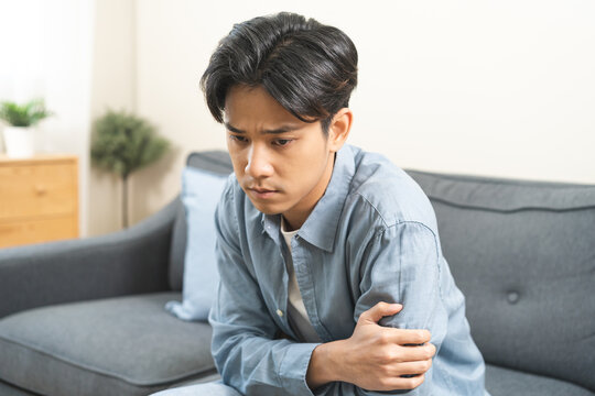 Sad unhappy, alone asian young man headache holding forehead thinking about problem, difficulty, feeling failure and exhausted, suffering sitting on sofa, grief sorrow and bad relationship or break up