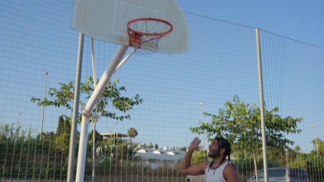 Young man performing slam dunk on outdoor basketball court