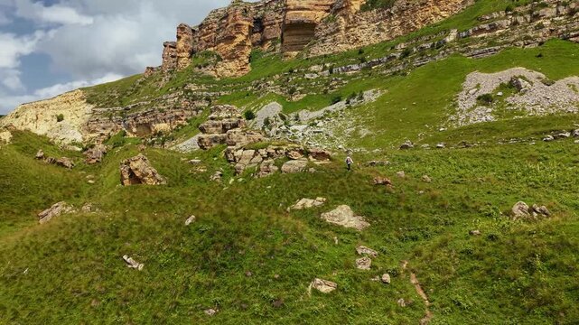 Person walking up a green mountain slope aerial view