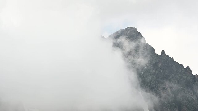 Dense clouds rolling over jagged rocky mountain peak
