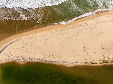 Aerial view of a sandy beach meeting the ocean with waves crashing on the shore and a calm river estuary in Pacitan, East Java, Indonesia.