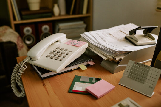 Retro office desk featuring vintage landline telephone, floppy disk, and paper documents. Concept of nostalgic corporate communication and old school business workflow, close up shot