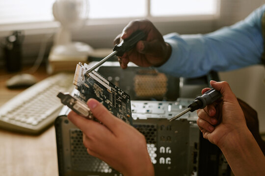 Hands of African American man and Caucasian woman repairing computer hardware in retro office. Close up shot suitable for tech support, vintage technology, and teamwork concepts