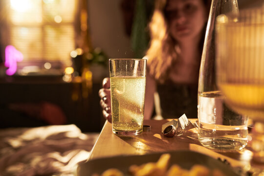 Young adult Caucasian woman reaching for glass of effervescent drink on table, representing hangover recovery or morning hydration. Ideal for wellness and pharmaceutical marketing campaigns
